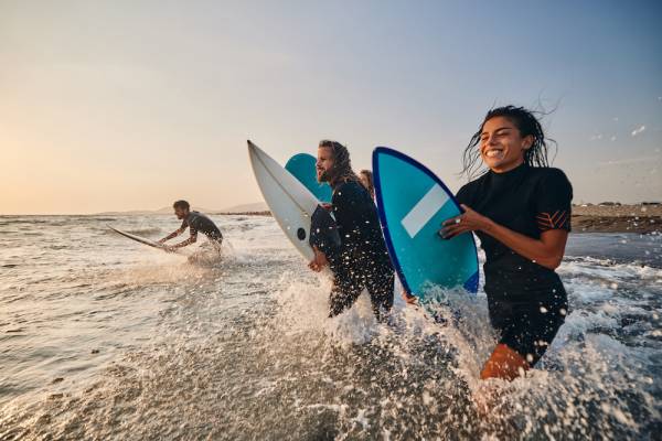 friends running into water with surfboards