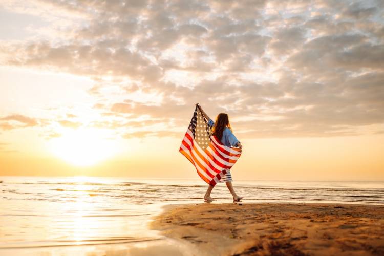 girl walking on the beach holding American flag over her back