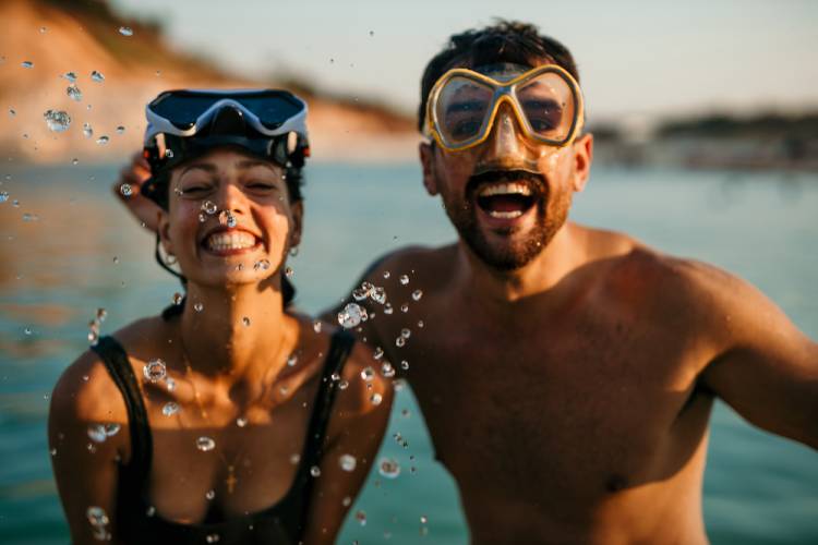 couple wearing snorkeling masks standing on the beach with ocean in background